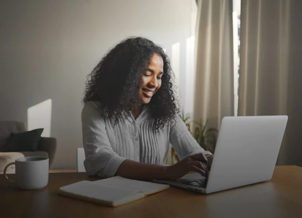 Mujer estudiante online de SNHU sentada, sonriendo y trabajando en una computadora